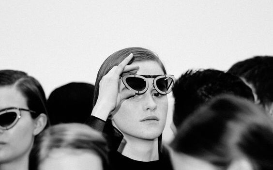 Black and white fashion portrait of a woman wearing sunglasses, standing out in a crowd, with a minimalist and artistic composition.